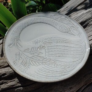May include: White ceramic plate featuring an embossed design of a bird with outstretched wings. The design is in a light grey colour and has a subtle texture.