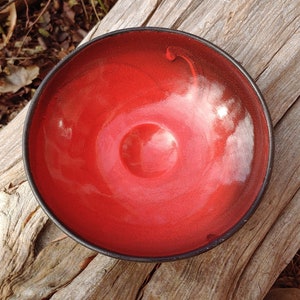May include: A red ceramic bowl with a black rim. The bowl has a glossy finish and a slight swirl pattern.