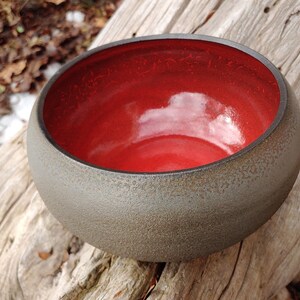 May include: A ceramic bowl with a dark gray exterior and a bright red interior. The bowl has a textured surface and a rounded shape.