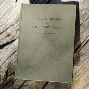 Puede incluir: Un libro antiguo con una cubierta verde apagada, titulado "ALL MY THOUGHTS & THE HEART TALKS" por C. CHICK DESIGN GRAPHICS. El libro descansa sobre una superficie de madera envejecida, con el t&iacute;tulo en una fuente simple y elegante.
