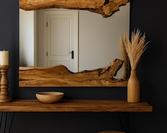 Puede incluir: Un espejo cuadrado grande con un marco de madera natural y un borde orgánico único. El espejo está montado sobre una consola de madera, complementada con un cuenco de madera, un candelabro y un jarrón con plantas secas. Un pequeño taburete de madera está frente a la mesa.