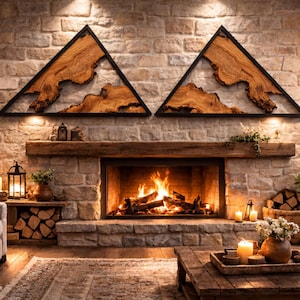 May include: A cozy living room scene featuring a stone fireplace with a roaring fire. Above the mantel are two triangular wooden wall art pieces with black frames. The room is decorated with candles, plants, and a wooden coffee table.