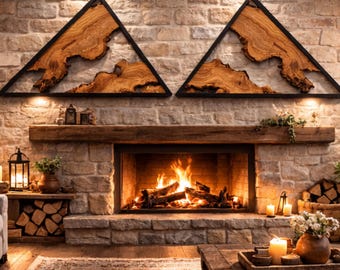 May include: A cozy living room scene featuring a stone fireplace with a roaring fire. Above the mantel are two triangular wooden wall art pieces with black frames. The room is decorated with candles, plants, and a wooden coffee table.