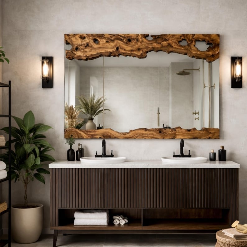 May include: A large rectangular mirror with a live edge wooden frame hangs above a double sink vanity. The vanity is dark brown with vertical grooves, and the countertop is white. Two black sconces flank the mirror.