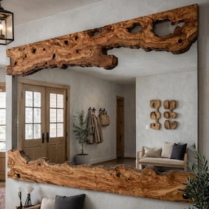 May include: A large rectangular mirror with a natural wood frame. The frame is made from a single piece of raw-edge wood, displaying the wood's grain and knots. The mirror is mounted on a light-coloured wall, reflecting the room's interior.