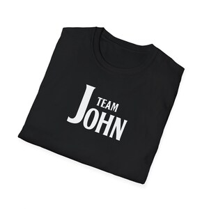 A folded black t-shirt angled on a white background, printed with white text that reads Team John.