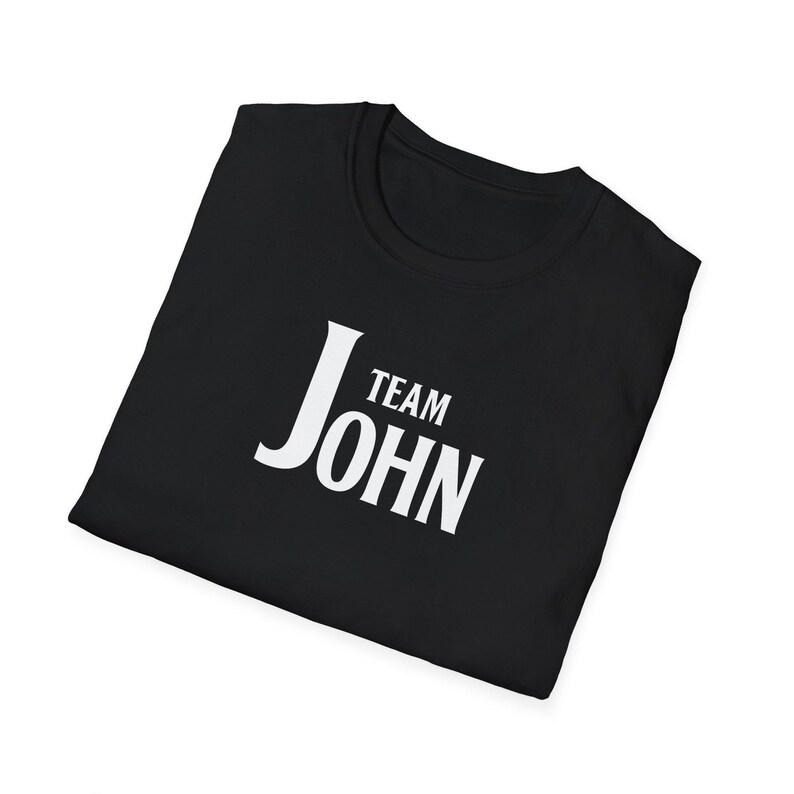 A folded black t-shirt angled on a white background, printed with white text that reads Team John.