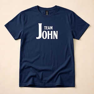 A navy blue crewneck t-shirt featuring the words Team John in white text on the chest, laid flat against a neutral background.