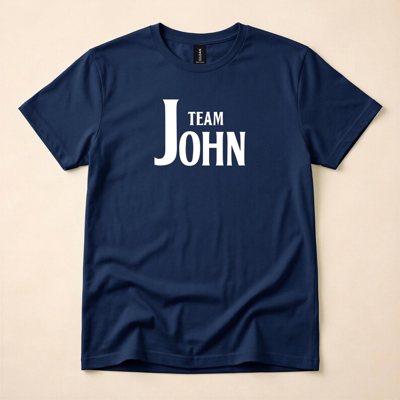 A navy blue crewneck t-shirt featuring the words Team John in white text on the chest, laid flat against a neutral background.