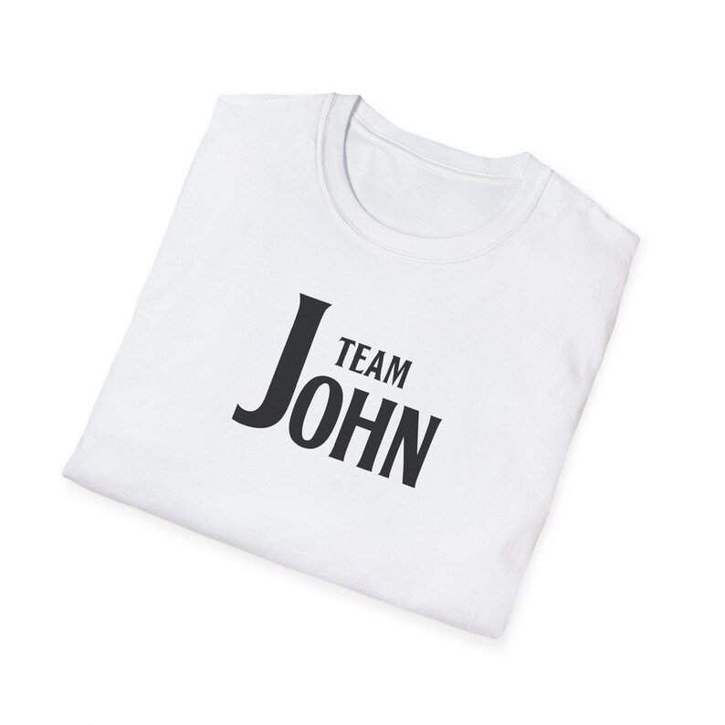 A folded white t-shirt angled on a white surface, featuring black text on the chest that reads Team John.
