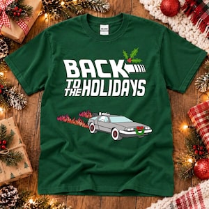 May include: A dark green short-sleeve t-shirt featuring the white text BACK TO THE HOLIDAYS with a holly sprig icon above it. Below the text is a graphic of a silver sports car with flames trailing behind and a green wreath on the front.