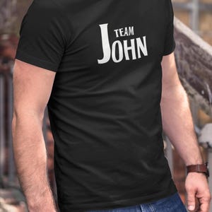 A person wearing a black t-shirt with Team John printed in white text on the front.
