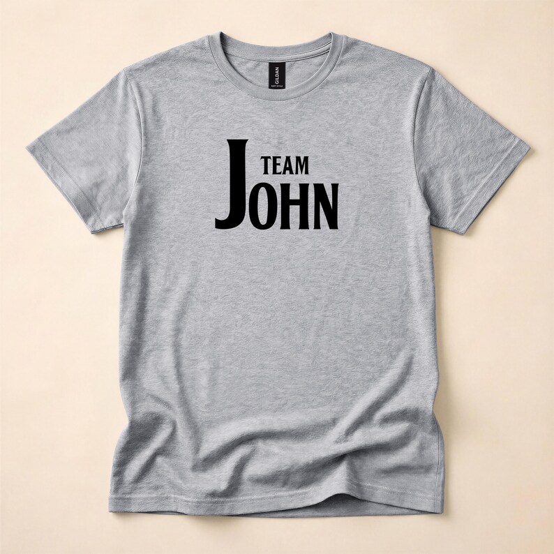 A heather grey crewneck t-shirt with Team John in black text printed on the front, laid flat against a neutral backdrop.