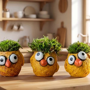 May include: Three whimsical, yellow owl-shaped planters with large white and black eyes and orange beaks. Each planter is filled with vibrant green moss. The planters are arranged on a wooden surface, suggesting a decorative or garden theme.