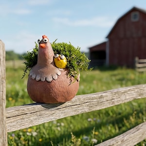 May include: A whimsical, brown ceramic hen planter with a yellow chick nestled inside, filled with green foliage. The hen has googly eyes and a red comb. The planter sits on a rustic wooden fence, with a red barn in the background.