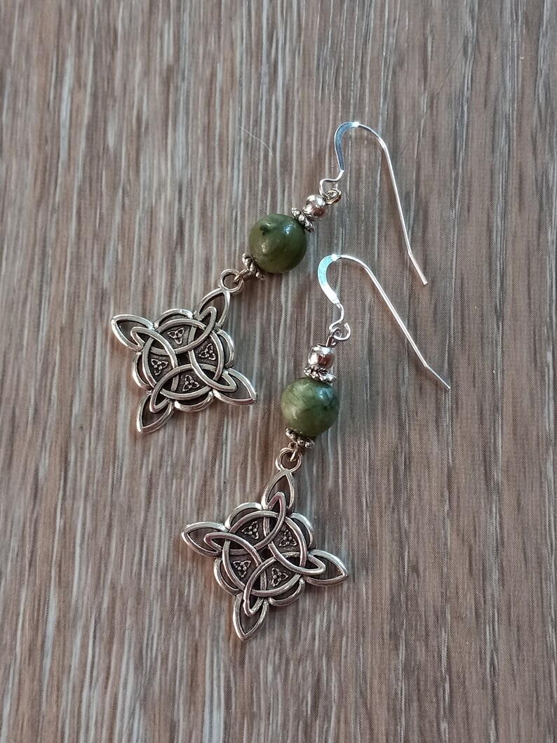 May include: A pair of silver-toned Celtic knot earrings with green stone beads. The earrings feature a four-leaf clover design with intricate knotwork. The ear wires are a simple hook style, and the beads are a muted green color.