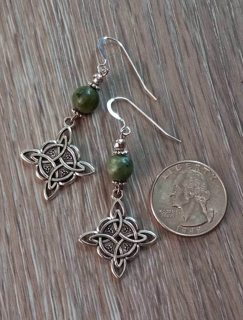 May include: A pair of silver-toned Celtic knot earrings with green stone beads. The earrings are displayed next to a U.S. quarter for size comparison. The earrings have a hook closure.