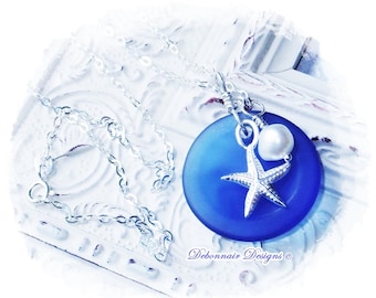 May include: A silver necklace featuring a blue pendant with a starfish charm and a white pearl. The pendant is round and has a smooth surface. The necklace is displayed on a white surface.
