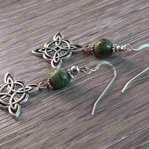 May include: Silver-toned Celtic knot earrings with green gemstone beads. The earrings feature intricate knotwork designs and are suspended from silver ear wires. The green beads add a pop of color to the jewelry.