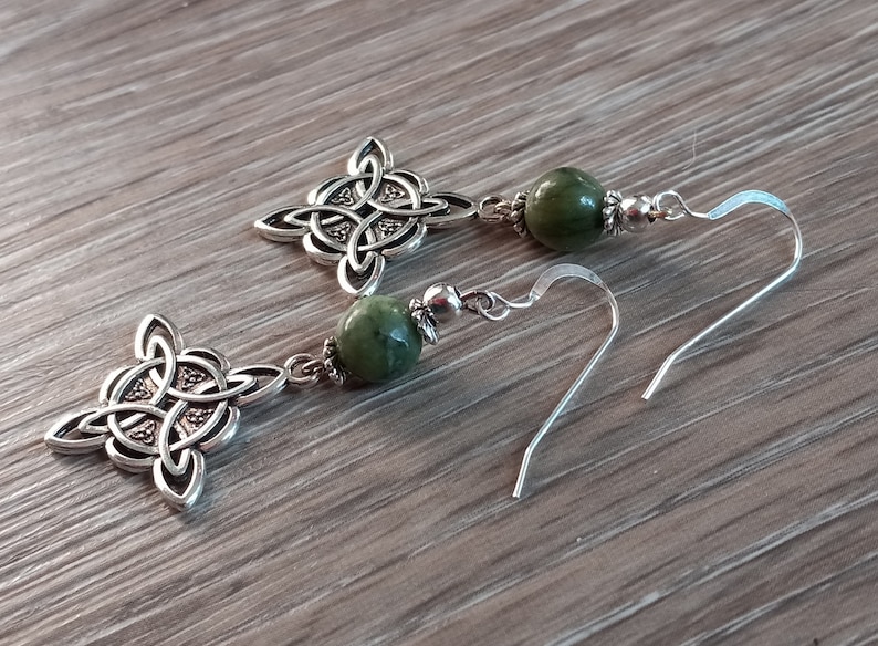 May include: Silver-toned Celtic knot earrings with green gemstone beads. The earrings feature intricate knotwork designs and are suspended from silver ear wires. The green beads add a pop of color to the jewelry.