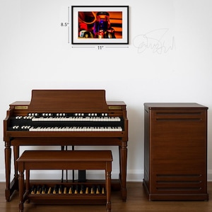 May include: A brown wooden organ with a matching bench and a framed picture on the wall. The picture is 11 inches wide and 8.5 inches tall. The organ has black and white keys and a foot pedal board.
