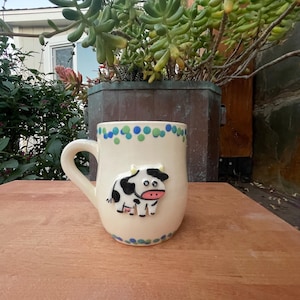 Op de afbeelding: Een witte keramische mok met een zwart handvat en de tekst "But First, Coffee" in een zwarte, vette letter. De mok staat op een wit oppervlak. De mok is 10 cm hoog.