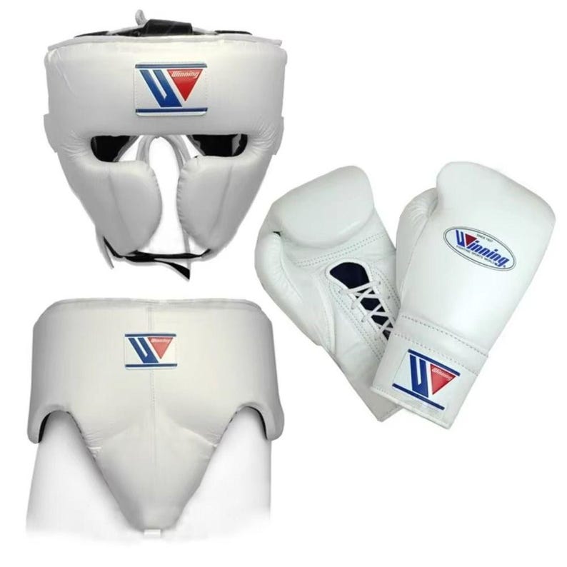 May include: A white boxing gear set consisting of a headgear, a groin protector, and a pair of lace-up boxing gloves. Each piece features the Winning logo with a blue and red graphic design. The equipment is constructed from white leather.
