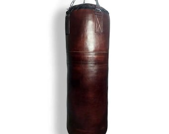May include: A dark brown leather punching bag suspended from a metal chain. The cylindrical bag is a deep brown colour and features stitched seams. Metal rings are attached to the top of the bag for chain attachment.