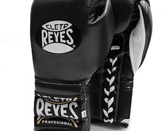 May include: Black leather boxing gloves with white laces and the text "Cleto Reyes" in a white oval on the front. The gloves also have a gold label with the text "Cleto Reyes Profesional" on the side.