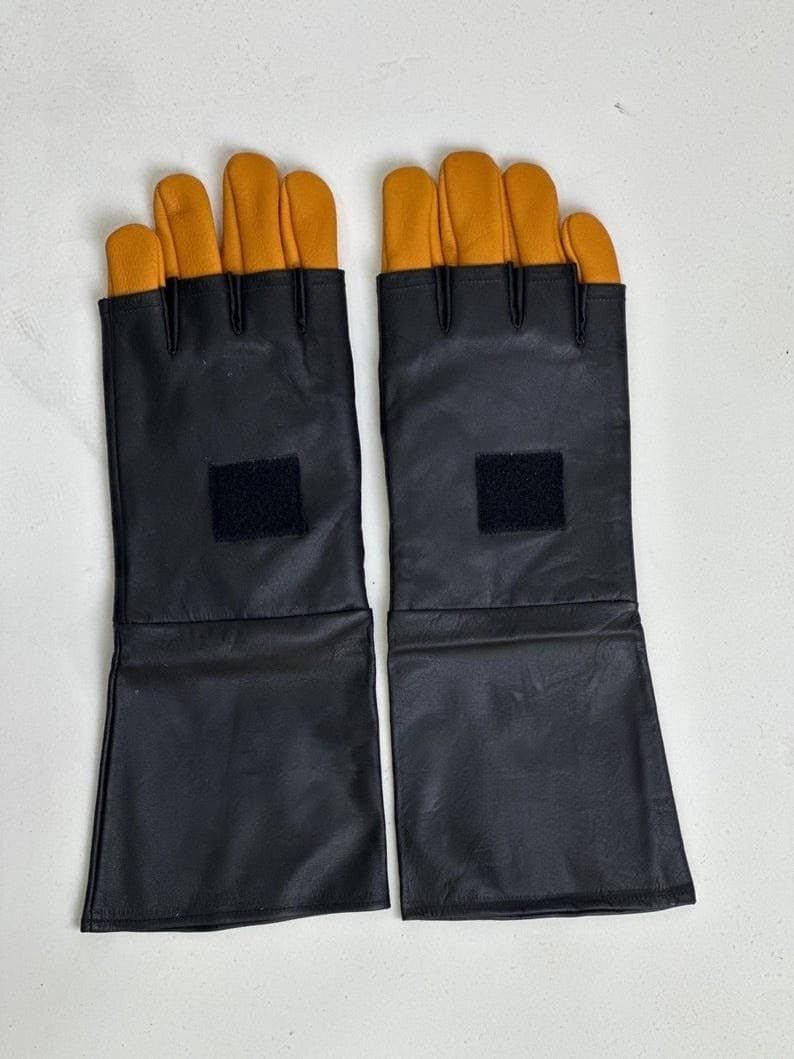 May include: A pair of fingerless gloves featuring long black leather cuffs and yellow leather fingers. Each glove has a square black hook-and-loop fastener patch centered on the back of the hand, extending from the wrist to the mid-forearm.