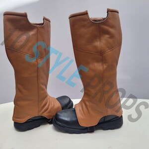 May include: A pair of knee-high boots featuring tan leather-like shafts and black rounded-toe bases. The boots have a distinct cutout at the top of the shaft and a strap across the foot. The text 1D STYLE PROPS is overlaid across the image.