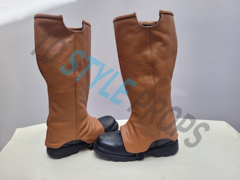 May include: A pair of knee-high boots featuring tan leather-like shafts and black rounded-toe bases. The boots have a distinct cutout at the top of the shaft and a strap across the foot. The text 1D STYLE PROPS is overlaid across the image.