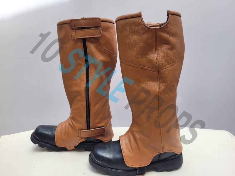 May include: A pair of knee-high gaiters featuring a tan leather upper section with black vertical zippers and adjustable hook-and-loop straps, paired with black rounded-toe boots that have thick, lugged rubber soles and the text 10 STYLE PROPS.