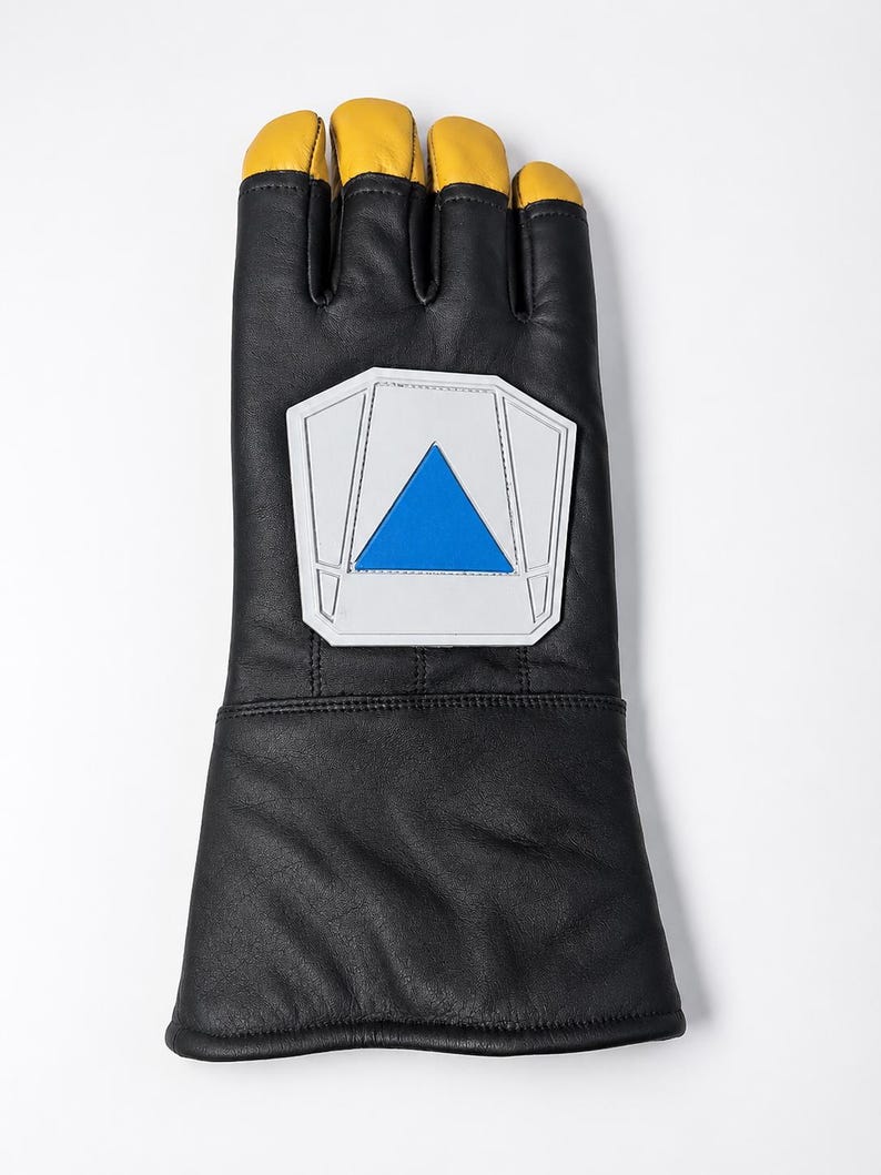 May include: A black leather gauntlet glove featuring yellow leather fingertips and a prominent white pentagonal patch on the back of the hand. The patch contains a centered blue triangle design with stitched detailing around the edges.
