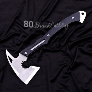 May include: A tactical axe with a black handle and a silver blade. The blade has a unique design with a circular cutout and a pointed edge. The text "80 Brand Cutlery" is visible on the image.