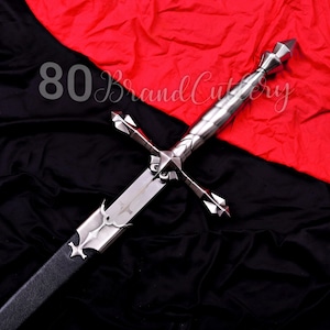 May include: A silver sword with a cross-shaped hilt and a black leather-wrapped handle. The blade is etched with a design. The background is a combination of red and black fabric. The text "80 Brand Cutlery" is visible.