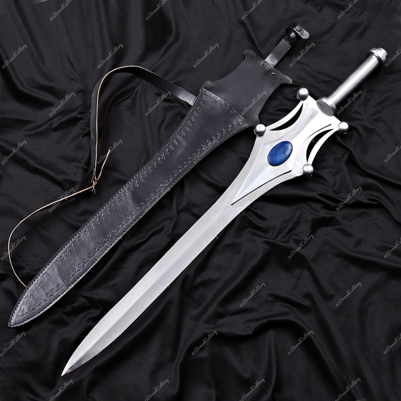 Puede incluir: Una espada plateada con una gema azul en la empu&ntilde;adura, junto a una vaina de cuero negro. La espada tiene un mango decorativo y una hoja larga y afilada. La vaina tiene una correa. La longitud de la espada es de aproximadamente 76 cm.