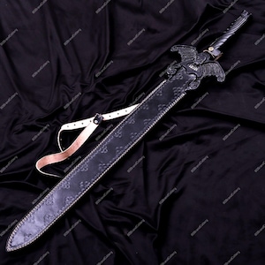 May include: A black sword with a decorative handle and a sheath. The sword features an ornate design with a winged emblem on the hilt. The sheath is black with a floral pattern and a white strap. The sword is displayed on a black fabric.
