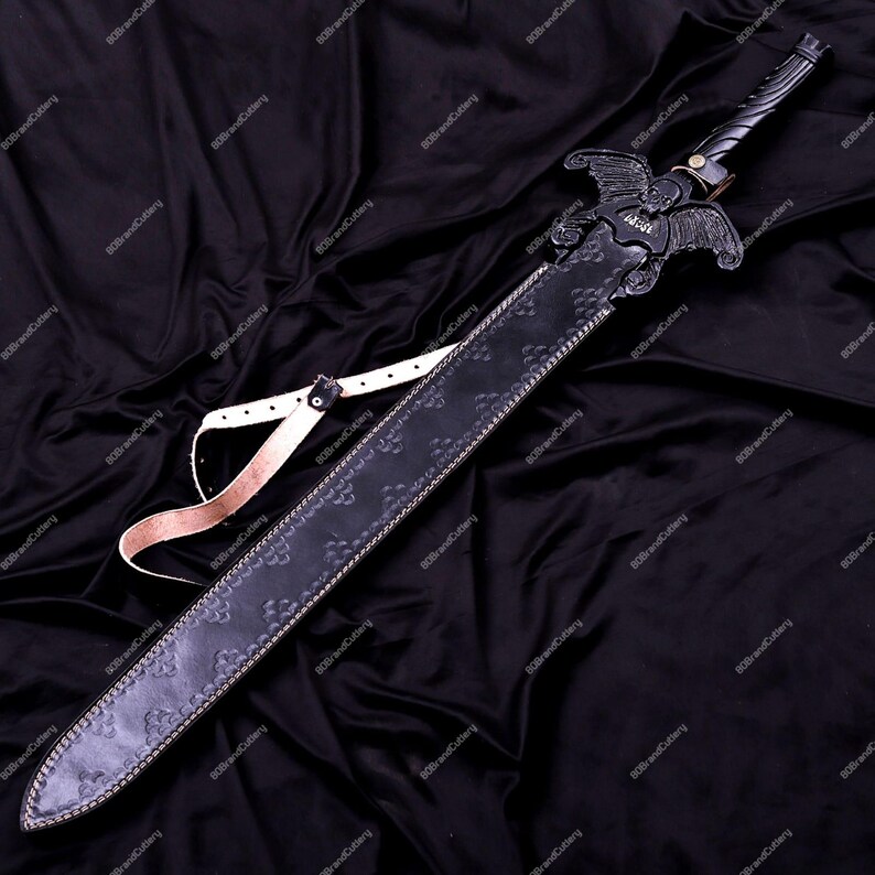 May include: A black sword with a decorative handle and a sheath. The sword features an ornate design with a winged emblem on the hilt. The sheath is black with a floral pattern and a white strap. The sword is displayed on a black fabric.