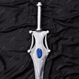 Puede incluir: Una espada plateada con un mango largo y cil&iacute;ndrico y una hoja decorativa. La hoja presenta una gema ovalada azul y detalles redondeados. La espada se muestra sobre un fondo oscuro y texturizado. Dise&ntilde;o de fantas&iacute;a.