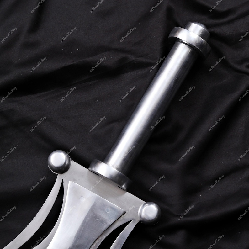 Puede incluir: Primer plano de una espada plateada con un mango y una hoja detallados. La espada tiene un mango cil&iacute;ndrico con un pomo redondeado y una guarda decorativa. La hoja es ancha y plana, con una punta. La espada est&aacute; sobre un fondo oscuro.