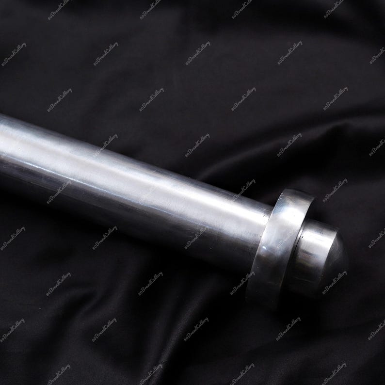 Puede incluir: Primer plano de un objeto met&aacute;lico cil&iacute;ndrico pulido, con un extremo redondeado y un detalle en forma de anillo. El objeto es plateado y parece estar hecho de acero o un metal similar. El fondo es una tela oscura y texturizada.