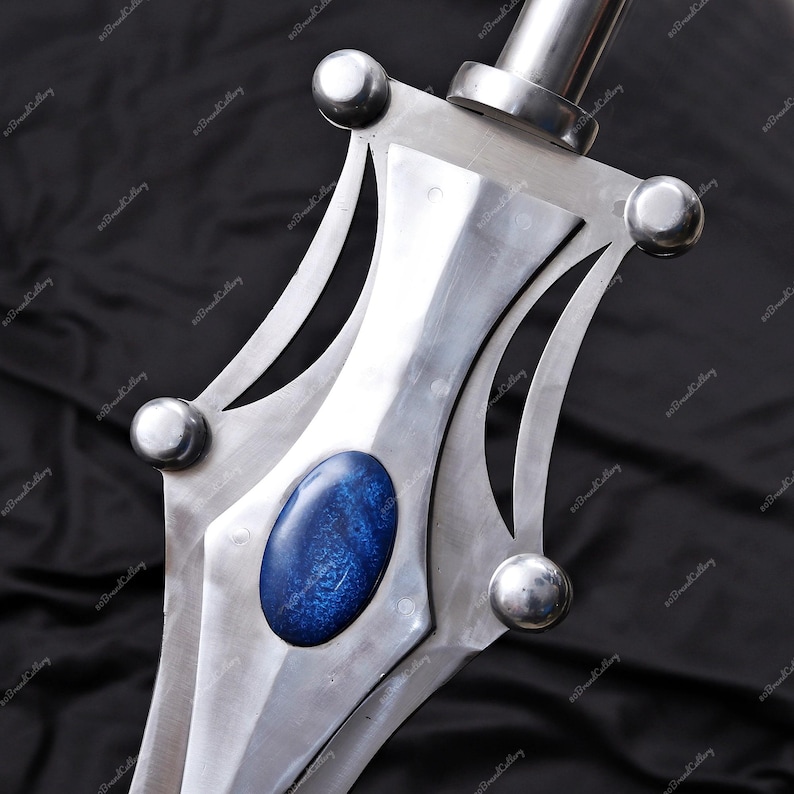 Puede incluir: Primer plano de una espada plateada con una piedra azul en el centro de la empu&ntilde;adura. La espada tiene un acabado pulido y detalles plateados redondeados. La hoja es afilada y el dise&ntilde;o es sim&eacute;trico.