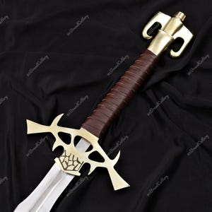 May include: A decorative sword with a polished steel blade and a gold-colored hilt. The handle is wrapped in brown leather. The sword features a unique design with a stylized crossguard and a detailed pommel. The overall length is approximately 30 inches.