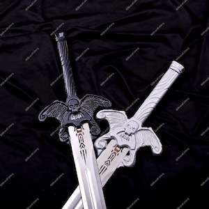 May include: Two decorative swords with silver blades and ornate handles. One sword is black, the other is silver. Both feature a skull and wing design on the crossguard and the word "CAUSE". The swords are displayed against a black background.