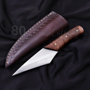 Puede incluir: Un cuchillo de hoja fija con una punta de acero plateado afilada y un mango de madera marrón pulida asegurado por tres pasadores de latón. El cuchillo viene acompañado de una funda de cuero marrón oscuro con costuras decorativas.