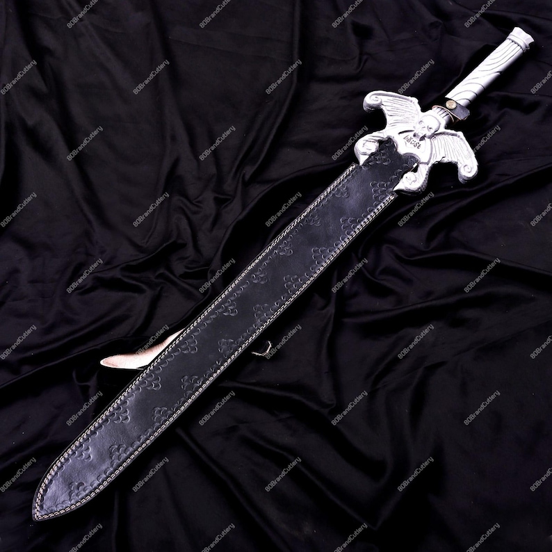 May include: A silver and black sword with a decorative hilt featuring a winged design. The sword is sheathed in a black leather scabbard with an embossed pattern and silver trim. The blade is visible at the tip.