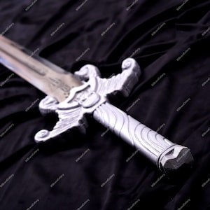 May include: A silver-colored sword with an ornate hilt and a detailed blade. The hilt features a decorative design with a shield-like emblem. The sword is set against a dark, textured background, highlighting its metallic sheen. A fantasy-themed item.