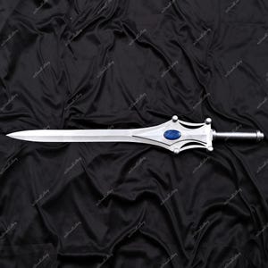 Puede incluir: Una espada plateada con una hoja puntiaguda y una guarda decorativa. La guarda presenta una gema ovalada azul y un mango plateado. La espada se muestra sobre un fondo negro texturizado.