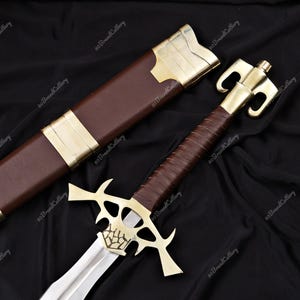 Könnte beinhalten: Ein dekoratives Schwert mit polierter Stahlklinge und Messinggriff. Der Griff ist mit braunem Leder umwickelt. Das Schwert wird von einer braunen Lederscheide mit Messingakzenten begleitet. Der Hintergrund ist ein dunkler Stoff.